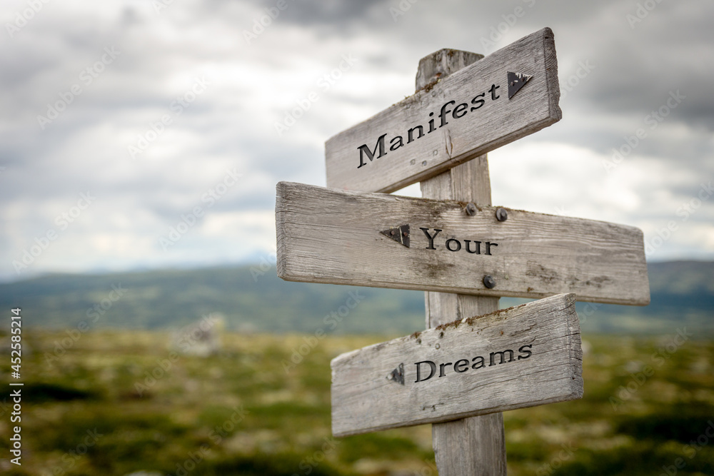 manifest your dreams text quote on wooden signpost outdoors in nature.